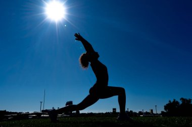 Şehir parkında gün doğumunda yoga yapan esnek kadın silueti.