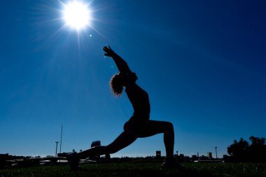 Şehir parkında gün doğumunda yoga yapan esnek kadın silueti.