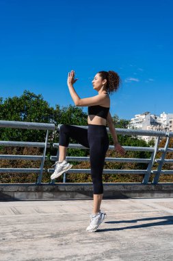 Açık havada egzersiz yaparken dizlerini çalıştıran sağlıklı bir kadın.