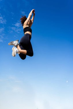 Fit bir kadın, canlı mavi gökyüzüne karşı yüksek atlama yapıyor. Atletizm ve özgürlük sergiliyor.