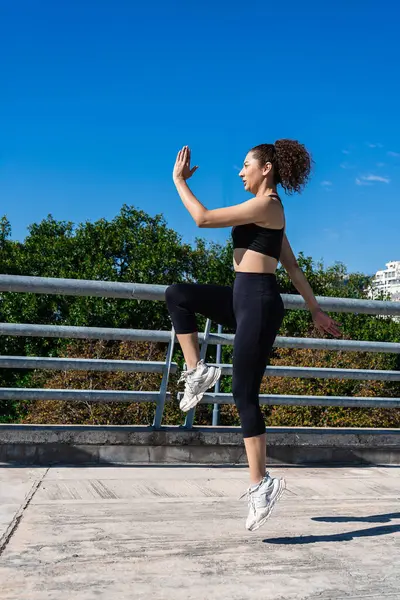 Açık havada egzersiz yaparken dizlerini çalıştıran sağlıklı bir kadın.