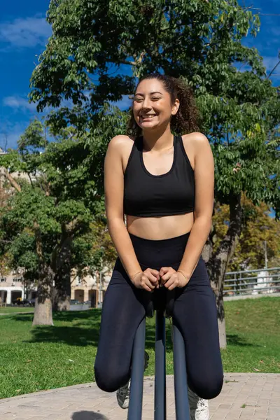 Mutlu atletik kadın antrenman sırasında mola veriyor, yeşil bir parkta güneşli havanın tadını çıkarıyor.