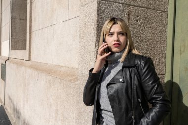 Güneşli bir günde duvara yaslanırken akıllı telefondan konuşan modaya uygun genç bir kadın.