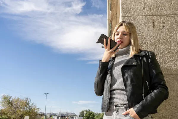 Şehirde duvara yaslanırken akıllı telefon kullanan şık bir genç kadın.