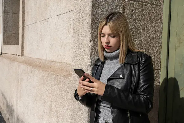 Şehirde duvara yaslanırken akıllı telefon kullanan şık bir genç kadın.