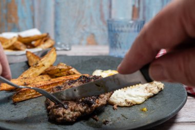 Eller ızgara bifteği çatal bıçakla keser, patates kızartması ve yumurta ile servis eder.