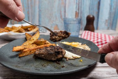 Elde çatal, hamburger bifteği, patates kızartması ve tabakta kızarmış yumurta.
