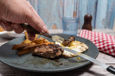 Kirli bir tabakta hamburger bifteği kesmek için çatal bıçak takımı ve kızarmış yumurta kullanılıyor, yemeye hazır.
