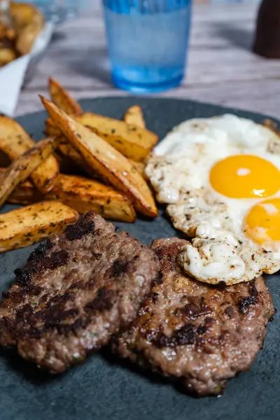 Kızarmış yumurta ve kızarmış patatesle servis edilen iki lezzetli ev yapımı hamburger doyurucu ve doyurucu bir yemek oluşturur.