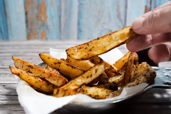 Parşömen kağıdıyla kaplı servis tabağından elde toplanan baharatlı patates dilimlerinin yakın çekimi.