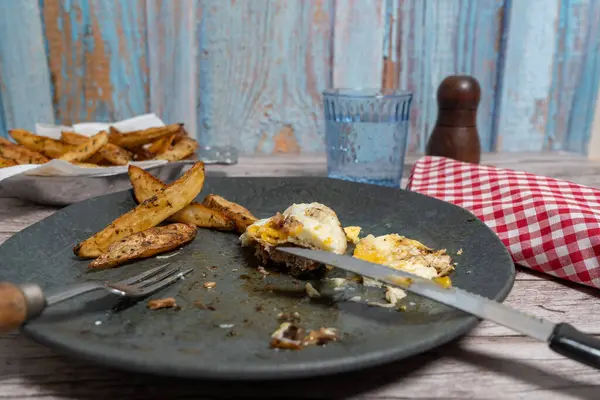 Kirli bir tabakta hamburger bifteği kesmek için çatal bıçak takımı ve kızarmış yumurta kullanılıyor, yemeye hazır.