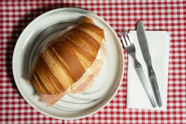 Sanatsal jambonlu ve peynirli kruvasan sandviçi, mükemmel bir şekilde kızartılmış ve kırsal ahşap tabakta servis ediliyor. Yemek fotoğrafçılığı ve markalaşma için harika..
