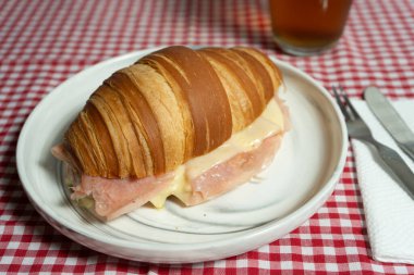Pahalı jambonlu ve erimiş peynirli taze pişmiş kruvasan sandviçi, altın kabuğunu ön plana çıkarıyor. Fırın siteleri ya da tarif gönderileri için mükemmel.