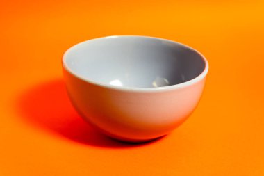 Canlı turuncu arka planda basit gri kase güçlü bir kontrastlık ve gölge oluşturur.