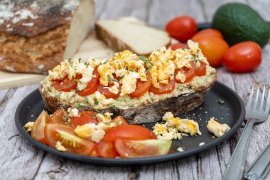 Avokado soslu ekmek, domates ve kırsal bir masada çırpılmış yumurta.