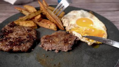 Yumurta sarısı hamburger ve patatesle servis edilen sahanda yumurtadan damlıyor.