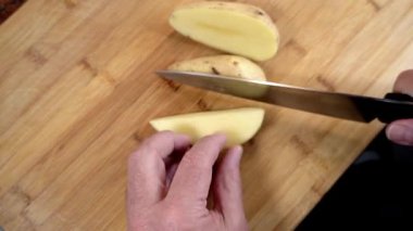 Şef patatesleri patates kızartması için hazırlıyor, onları tahta bir tahtanın üzerinde sopayla kesiyor.