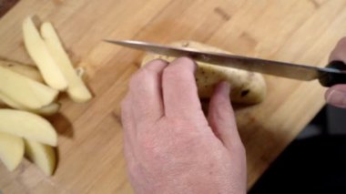 Eller ustalıkla bir patatesi tahta kesme tahtasıyla dilimliyor.