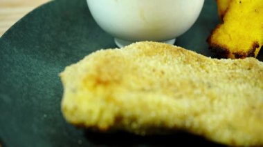 Ekmek arası tavuk göğsü, polenta ve beyaz sos enfes bir mutfak sahnesi yaratıyor.