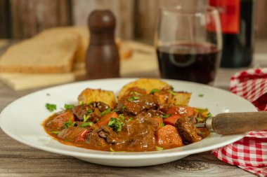 Patates ve bir bardak kırmızı şarapla servis edilen tuzlu biftek güveci.
