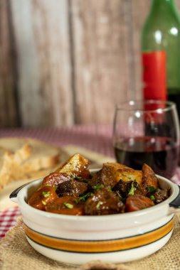 Kırmızı şarap ve taze ekmekle servis edilen etli güveç.