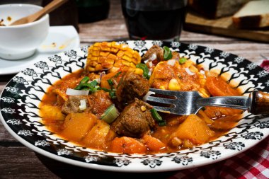 Yürekli et yahnisi, tereyağlı kabak, koçanda mısır ve doğranmış yeşil soğanla süslenmiş havuç, dekoratif bir kasede servis ediliyor.