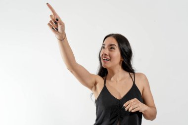 Heyecanlı genç bir kadın beyaz arka planda ilginç bir şeyi işaret ediyor.