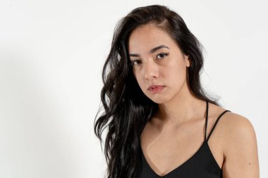 Uzun, koyu renk saçlı, siyah bluz giyen, ciddi ve düşünceli bir ifade sergileyen genç bir Latin kadının stüdyo portresi.