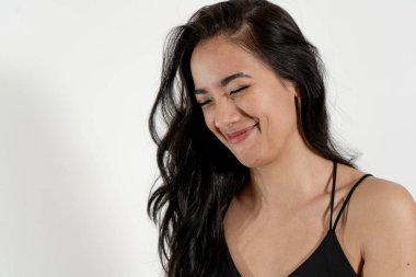 Uzun siyah saçlı, siyah bluzlu, gözleri kapalı ve başı eğik gülümseyen neşeli genç bir kadının stüdyo portresi.