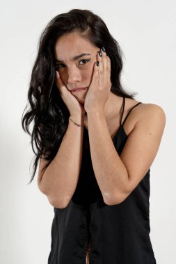 Uzun siyah saçlı, elleriyle yüzünü tutan endişeli genç bir kadının stüdyo resmi.