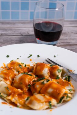 Maydanozla süslenmiş, domates sosuyla kaplanmış, beyaz bir tabakta servis edilen lezzetli ravioli makarnası.