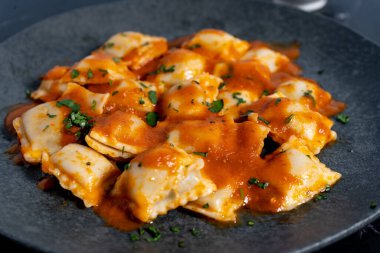 Lezzetli domates soslu ravioli makarna ve taze maydanoz, koyu bir tabakta servis edilir.