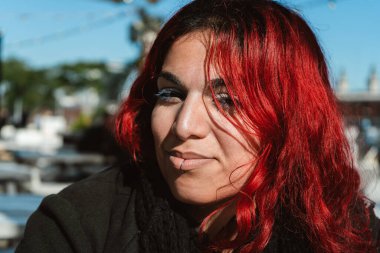 Açık havada güneşli bir günün tadını çıkaran parlak kızıl saçlı ve dudağına piercing takan hoş bir genç kadının portresi.