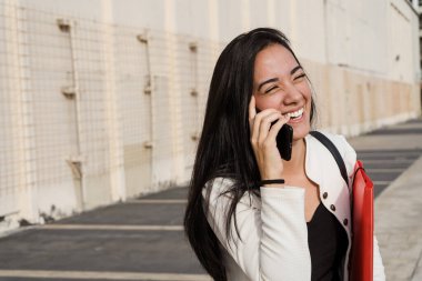 Elinde klasörler olan mutlu bir kız öğrenci ve akıllı bir telefonla konuşuyor, dışarıda güzel bir sohbetin tadını çıkarıyor.