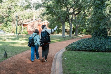 Genç çift el ele tutuşup, bir botanik bahçesinde yürüyor, yemyeşil otlakların arasında romantik bir gezinti yapıyorlar.