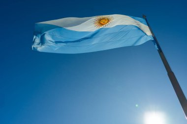 Arjantin bayrağı rüzgarda gururla dalgalanır açık mavi gökyüzüne karşı, güneş tarafından aydınlatılır