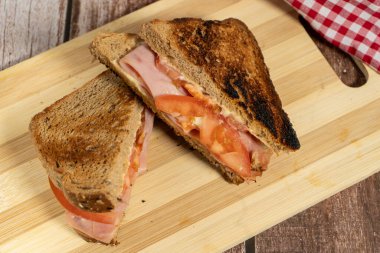 Tahta kesme tahtasında servis edilen dilimlenmiş domatesli kızarmış jambonlu peynirli sandviç.