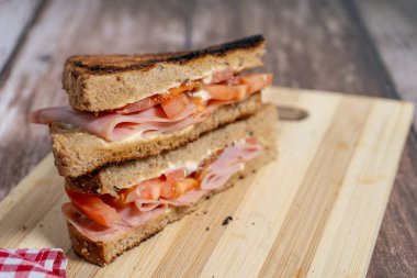 Kızarmış jambonlu ve domatesli sandviç ve tam buğday ekmekli mayonez, ahşap bir kesim tahtasının üzerinde sunuluyor.
