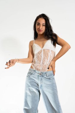 Beyaz elbiseli ve kot pantolonlu genç Latin kadın güven ve tavır sergiliyor.