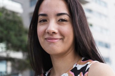 Uzun siyah saçlı neşeli genç bir kadının portresi, şehirde bir anın tadını çıkarıyor.