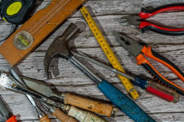 Pençe çekici, keski, pense, tornavida, katlama cetveli, mezura ve ruh seviyesi ahşap bir tezgahta yatıyor.