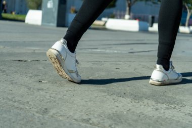 Beton zeminde yürüyen, beyaz spor ayakkabılar ve siyah taytlar giyen, kentsel aktiviteleri ve ayakkabıları vurgulayan kadınların yakın çekimleri