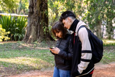 İki öğrenci parkta akıllı telefon kullanıyor. Doğanın ve teknolojinin tadını çıkarıyorlar.