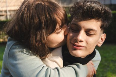 Romantik çift açık havada hassas bir anı paylaşıyor, kucaklaşıyor ve yanaktan öpüşüyorlar.