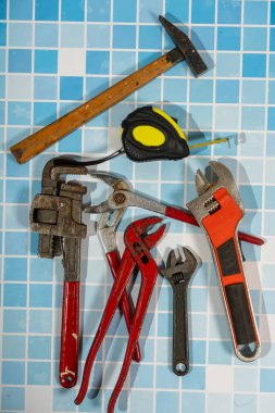 Çekiç, kerpeten, boru anahtarı ve mavi banyoda duran mezura gibi çeşitli tesisat aletleri.