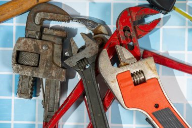 Mavi banyo fayanslarının üzerinde tesisatçının ev tamiri için kullanacağı çeşitli tesisat aletleri var.