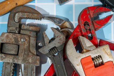 Birçok iyi kullanılmış anahtar ve boru anahtarı mavi fayansların üzerinde duruyor, aşınma ve yırtık izleri var.