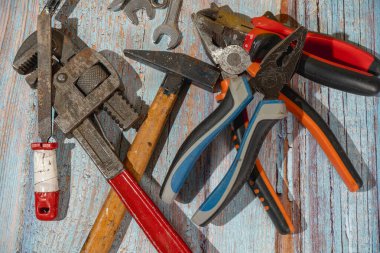 Pençe çekici, pense, ayarlanabilir anahtar ve diğer el aletleri atölyede kullanılmak üzere ahşap bir masada duruyor.