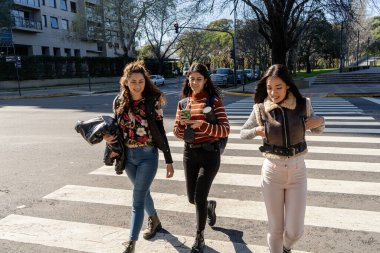 Güneşli bir günde, üç kız öğrenci yaya geçidinde yürüyor ve sohbet ediyorlar.