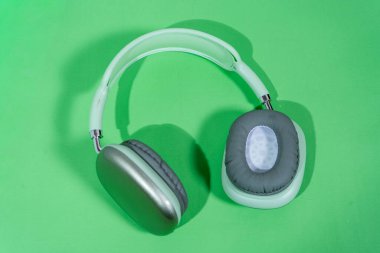 Canlı yeşil bir fon üzerinde dinlenen şık kulaklıklar, müziği, podcast dinlemeyi veya ses üretimini temsil ediyor.